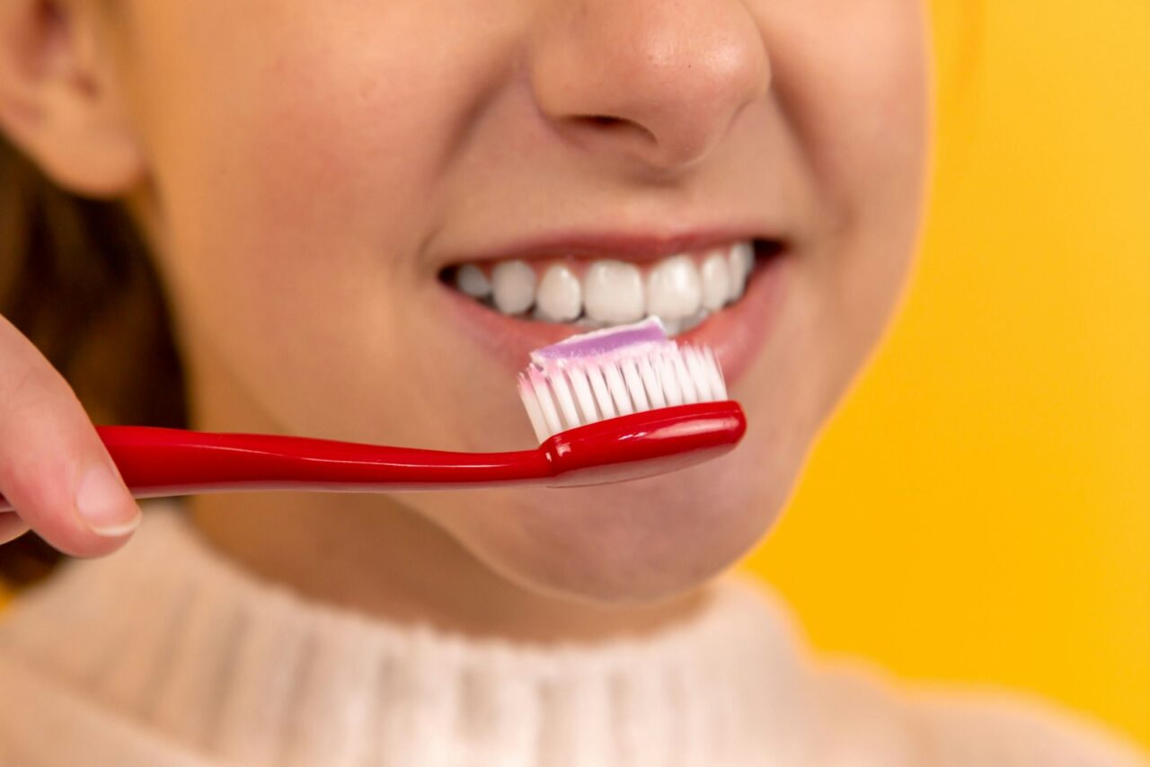 Person brushing their teeth in front of a bathroom mirror as part of a daily dental care routine