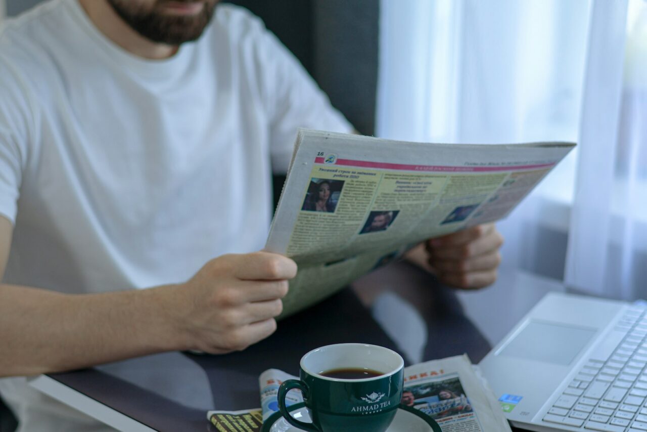 A person reading a newspaper at a cafe table with a cup of coffee