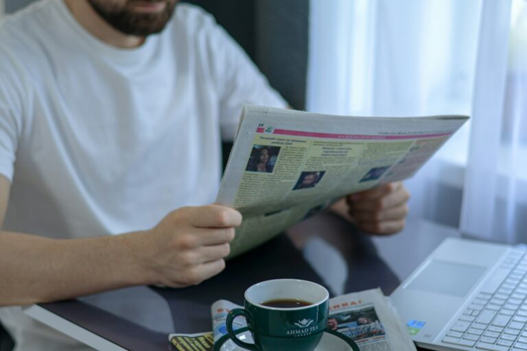 A person reading a newspaper at a cafe table with a cup of coffee
