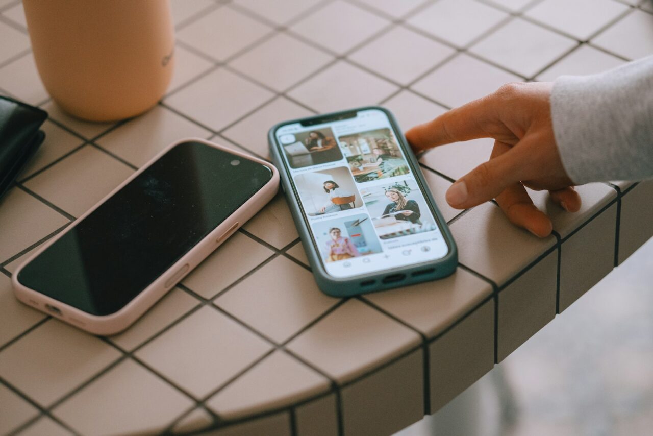 A smartphone placed face down on a wooden table next to a cup of coffee and a notebook
